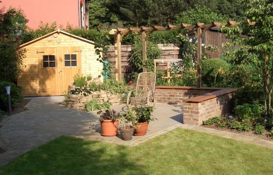 Gartengestaltung mit Pflasterung, Gartenhaus und Natursteinmauer